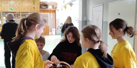 Powiększ grafikę: 3 dziewczyny w żółtych koszulkach trzymające koszyk z ciastkami. Obok uczennica kupująca ciasteczka.