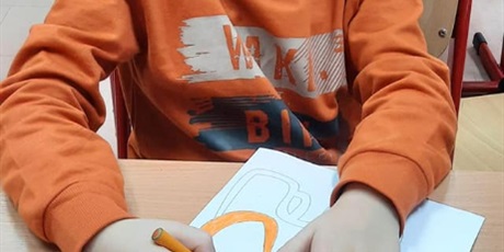 Powiększ grafikę: Chłopiec ubrany na pomarańczowo koloruje rysunek słonika Tumbo na pomarańczowo.