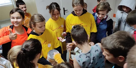Powiększ grafikę: Wolontariusze z klasy ubrani w żółte koszulki sprzedają ciasteczka. Obok dzieci kupujące
