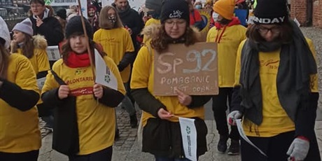 Powiększ grafikę: Grupa młodych ludzi w żółtych koszulkach podczas parady ulicami Gdańska nisąca kartonik z napisem: SP 92 pomaganie jest dobre!"