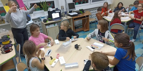 Powiększ grafikę: Grupydzieci siedzące przy stolikach, słuchające objaśnień jak używa się długopisy 3D.